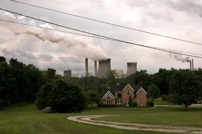 Smoke stacks billowing behind a large house and a grassy field.