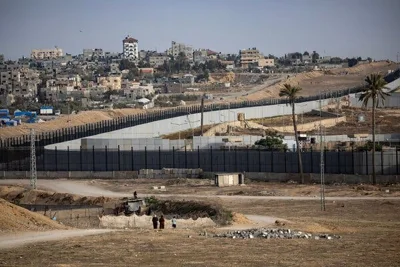 A border fence, with a cluster of buildings in the background.