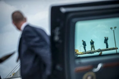 A member of the Secret Service holds a limo door open.