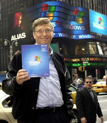 Standing in Times Square, a smiling Bill Gates holds up a copy of the Windows XP operating system. 