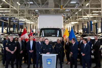 A group of people, some wearing suits, others wearing police uniforms, standing in front of a white truck.