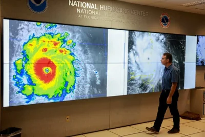 A man examines a colorful satellite image of Hurricane Beryl.