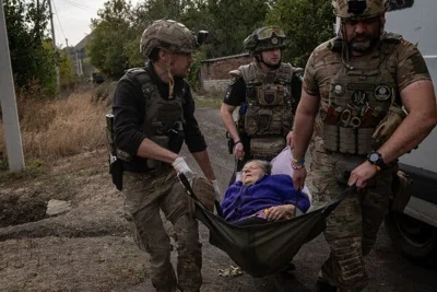 Three men in uniform and helmets carrying a women in a piece of cloth.