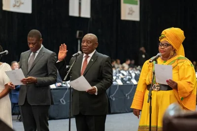 Cyril Ramaphosa standing behind a microphone and raising his right hand.