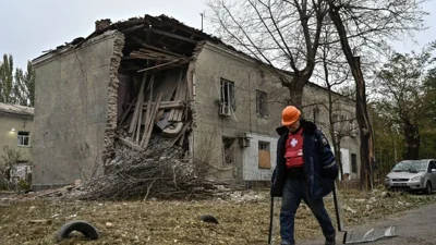 A municipal worker carries broken glass as he walks past an apartment building hit by a Russian air strike,